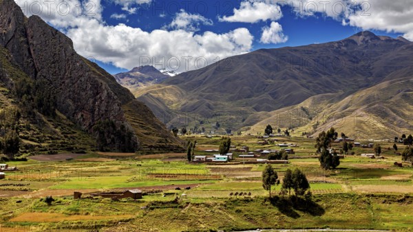 Green fields and hills against a mountain backdrop under a cloudy blue sky, the landscape in the