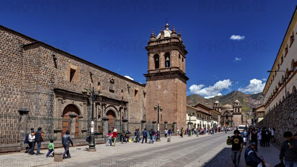 Historic street with impressive bell tower and mountain views, lively with passers-by in clear
