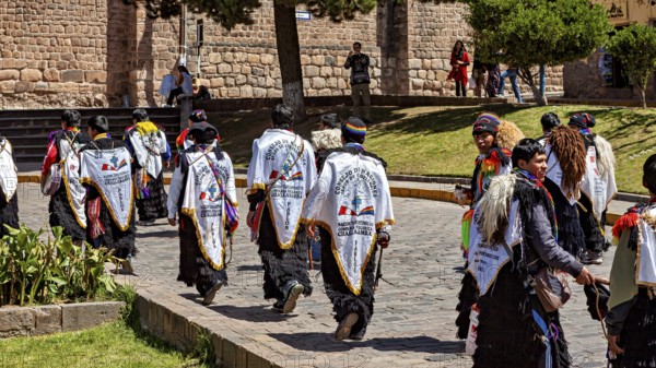 Group of people in white robes with back lettering move down the street during a procession,
