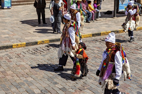 People in traditional costumes, including a child, on a paved street, traditional parade of