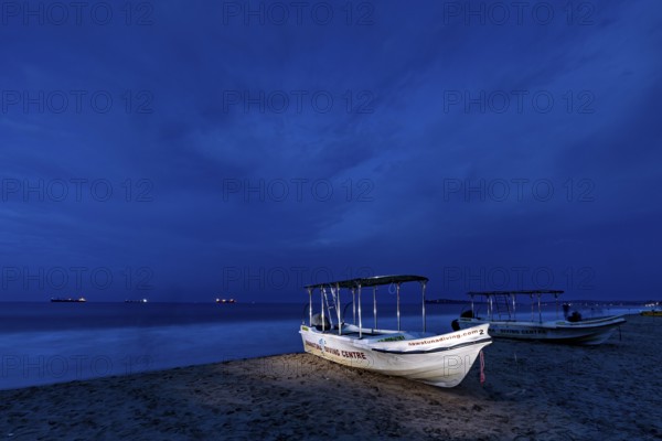 Night landscape with illuminated boat on beach, calm sea and dark sky, traditional boats on