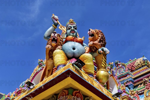 Colourful sculpture of a mythological being with lions on a temple against a blue sky, The Sri