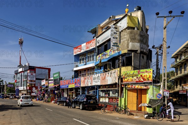 Busy urban street with shops and advertising signs under clear skies, the city of Trincomalee in