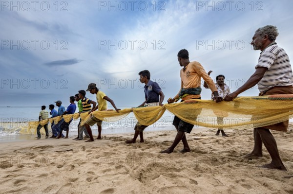 A group works together on the beach to pull a fishing net out of the water, Traditional fishermen