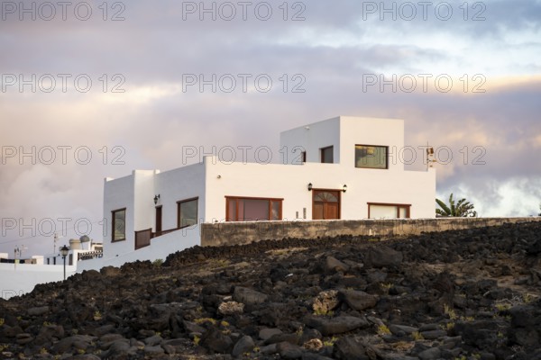 Black coast of volcanic rocks behind typical white houses of the village of La Santa, at sunset,