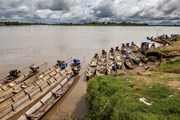 Wooden boats lie on the riverbank under a cloudy sky surrounded by lush greenery, longboat on a