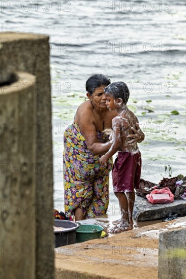 A woman washes a child at the river, both laugh and wear colorful clothes, a woman washes at a lake