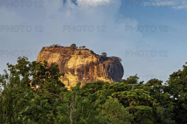 Massive rock juts out of the green landscape under a blue sky, The Lion Rock near Sigiriya in Sri