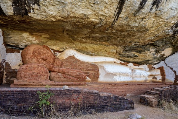 Ancient sandstone sculpture of a Buddha reclining under a rocky outcrop, tranquil setting, The