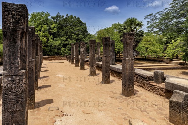 Row of open-air stone pillars on a sunny brick path with trees, The temples of Polonnaruwa in Sri