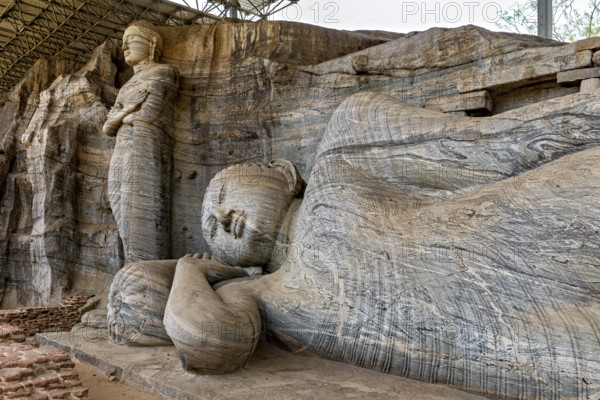 Close-up of the artistic detail of a large reclining Buddha statue next to a standing figure carved