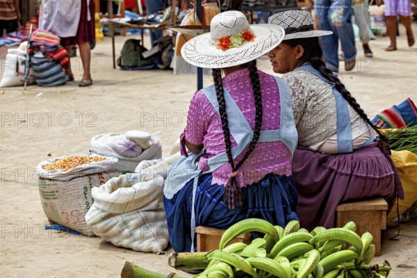 Two woman wearing hats and traditional dresses discuss their market status, The Rurrenabaque market