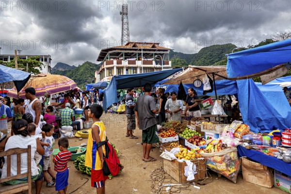 A bustling market with fruit and stalls under ominous clouds and mountain scenery, The Rurrenabaque