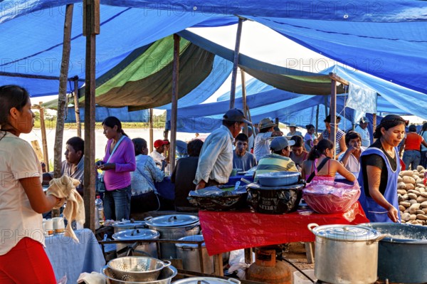 People cook and serve food under blue tarps in a busy market atmosphere, The Rurrenabaque market in