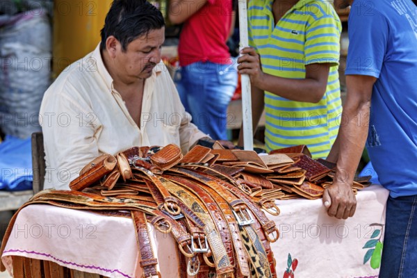 A man sells leather belts at a market stall surrounded by customers, The Rurrenabaque market in