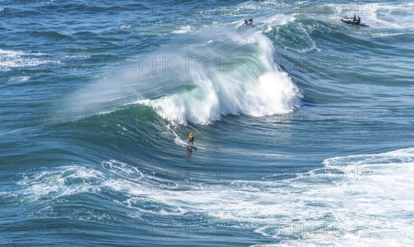 Surfers with their jet ski pilots in the Atlantic waves below Farol de Nazaré, Forte São Miguel,