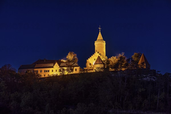 Illuminated castle at night, on a hill, surrounded by shadows and a bright blue night sky, The