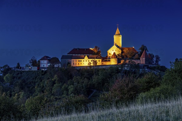 A castle at dusk, illuminated and picturesquely situated on a hill, in contrast to a clear blue