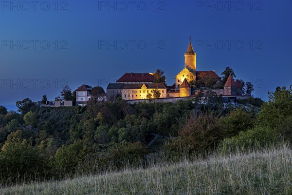 A castle on a wooded hill, illuminated at dusk with dark skies, The Leuchtenburg near Kahla im
