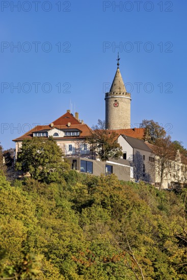 A castle with a distinctive tower, surrounded by colorful autumn trees against a clear sky, The