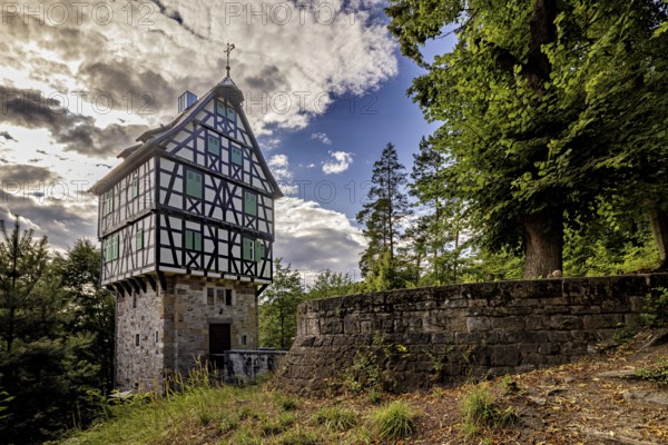 Half-timbered house on a stone base next to a stone wall in the forest, picturesquely illuminated