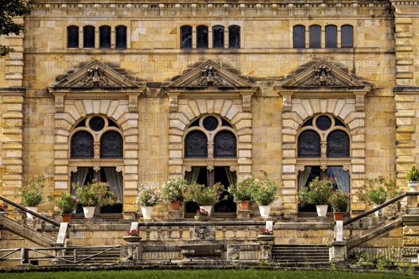 Detail of the castle façade with lush flowers in pots in front of large windows, The Hummelshain