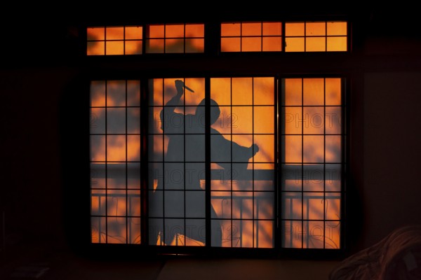Shadow of a man, burglar with knife, assassin, ninja, on the balcony behind sliding shoji doors in