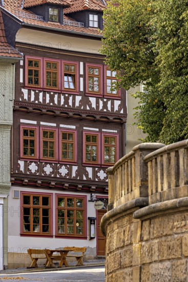 A half-timbered house with red window frames next to a stone wall in a historic town, The old town