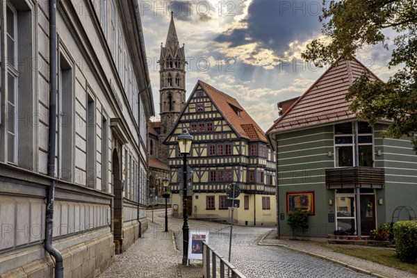 Paved street with half-timbered houses and church tower under a cloudy sky, the old town of