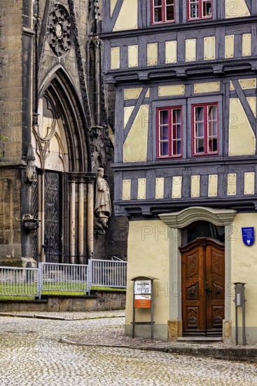 Detailed view of a church portal next to a half-timbered house, paved street in front of it, the