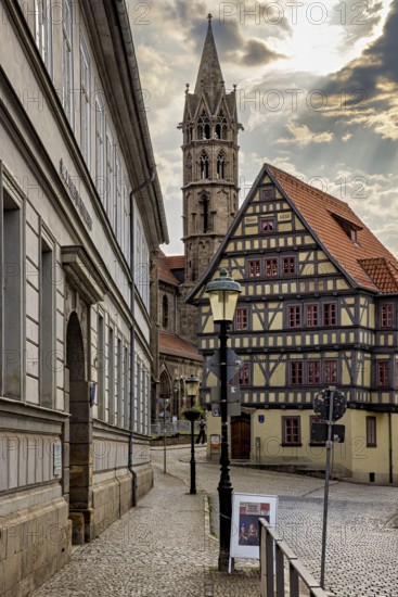 Alley with a view of a half-timbered house and a church tower, under a cloudy sky, the old town of