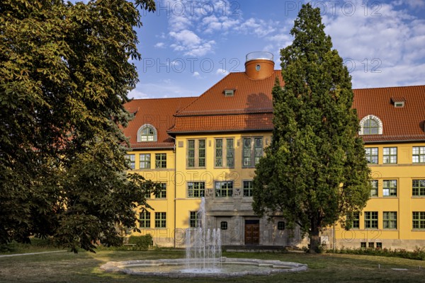 Large yellow building with surrounding garden, fountain and summer backdrop, the old town of
