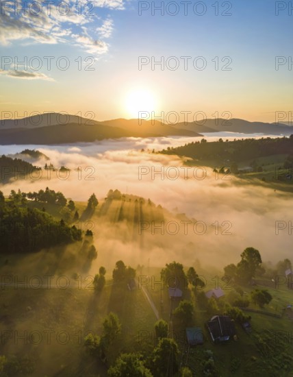 Sunrise over a fog covered village in a rural landscape, golden morning light, serene autumn