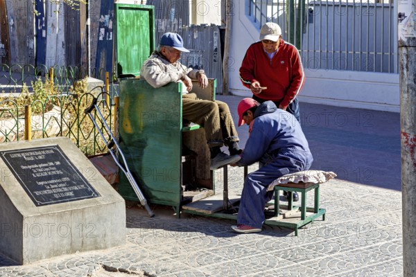 Three men interact in a relaxed street scene at a shoe shiner in the old town, show shiners in the