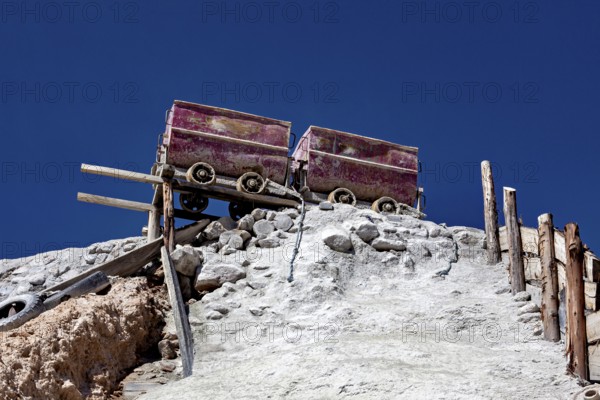 Two old mine cars standing on a rocky structure above a stony slope under a clear sky, mining lore