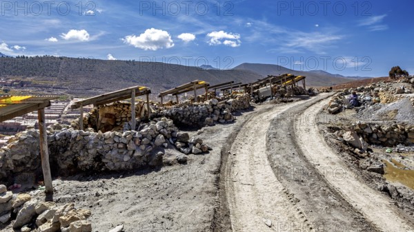 Dusty path with piles of stones next to a mountainous landscape under a blue sky with clouds, The