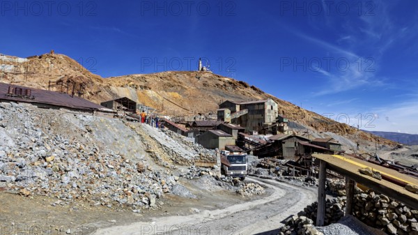 Old industrial complex in a mountainous environment under a clear blue sky with a visible path, The