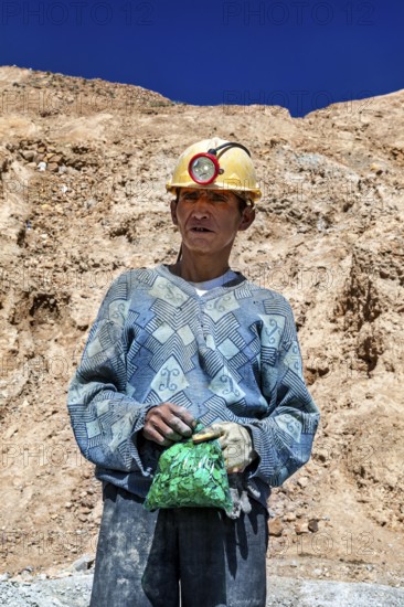 A man in a helmet and patterned jumper stands in front of a rocky landscape, The miners of the