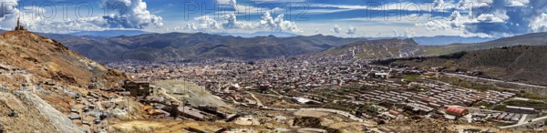 Expansive panorama of an urban landscape embedded in mountainous surroundings under a blue sky,