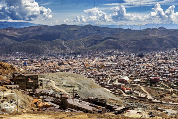 City view with surrounding mountains and numerous buildings under a cloudy sky, The silver mines of