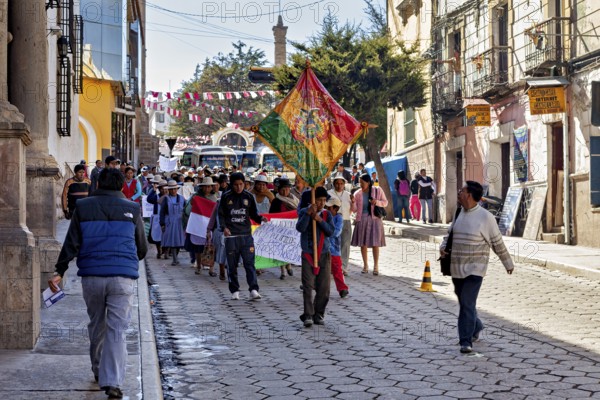 People demonstrate with flags and banners on a cobbled street between historic buildings,