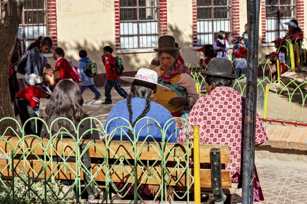 Women in traditional dress sit in the park while children play, people of the town of Uyuni in the