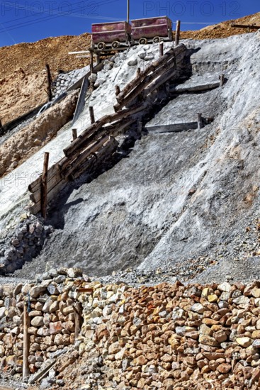 A lonely mine car stands on a rocky slope, surrounded by staggered layers of rock and wooden beams,
