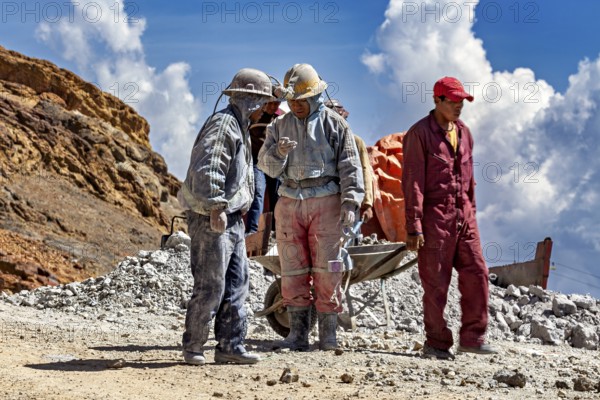 A group of miners stand and chat in a rocky landscape, The miners of the Cerro Rico silver mountain