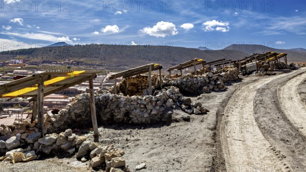 A dirt track leads through a dry, stony landscape under a blue sky with clouds, The silver mines of