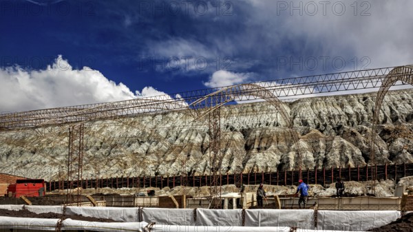 Industrial scene with scaffolding in front of a barren rock formation under a blue sky, slag heap