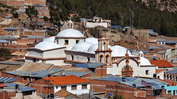 A city view with domes of a church in the foreground, surrounded by brick houses in a mountainous