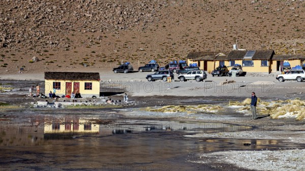 Huts and vehicles in a mountainous landscape with people, The thermal springs of Polques in Bolivia