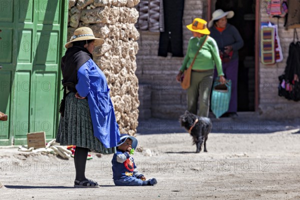 Woman and child in traditional dress stand with a dog in front of a green door in the village,