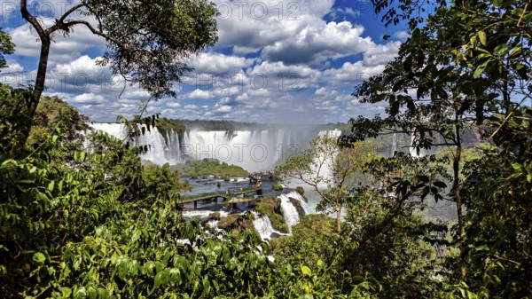 Lush green surroundings, waterfalls in the background, viewpoint with visitors, The Iguazu Falls